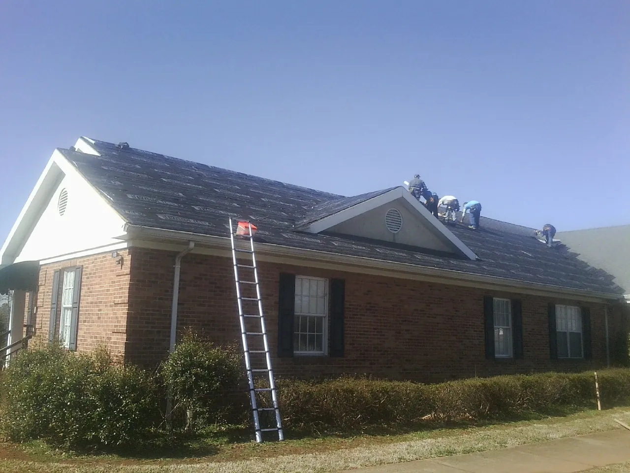 Crew tearing shingles off a brick ranch roof with a ladder set — Metal Roof Repair work by our crew in Kershaw