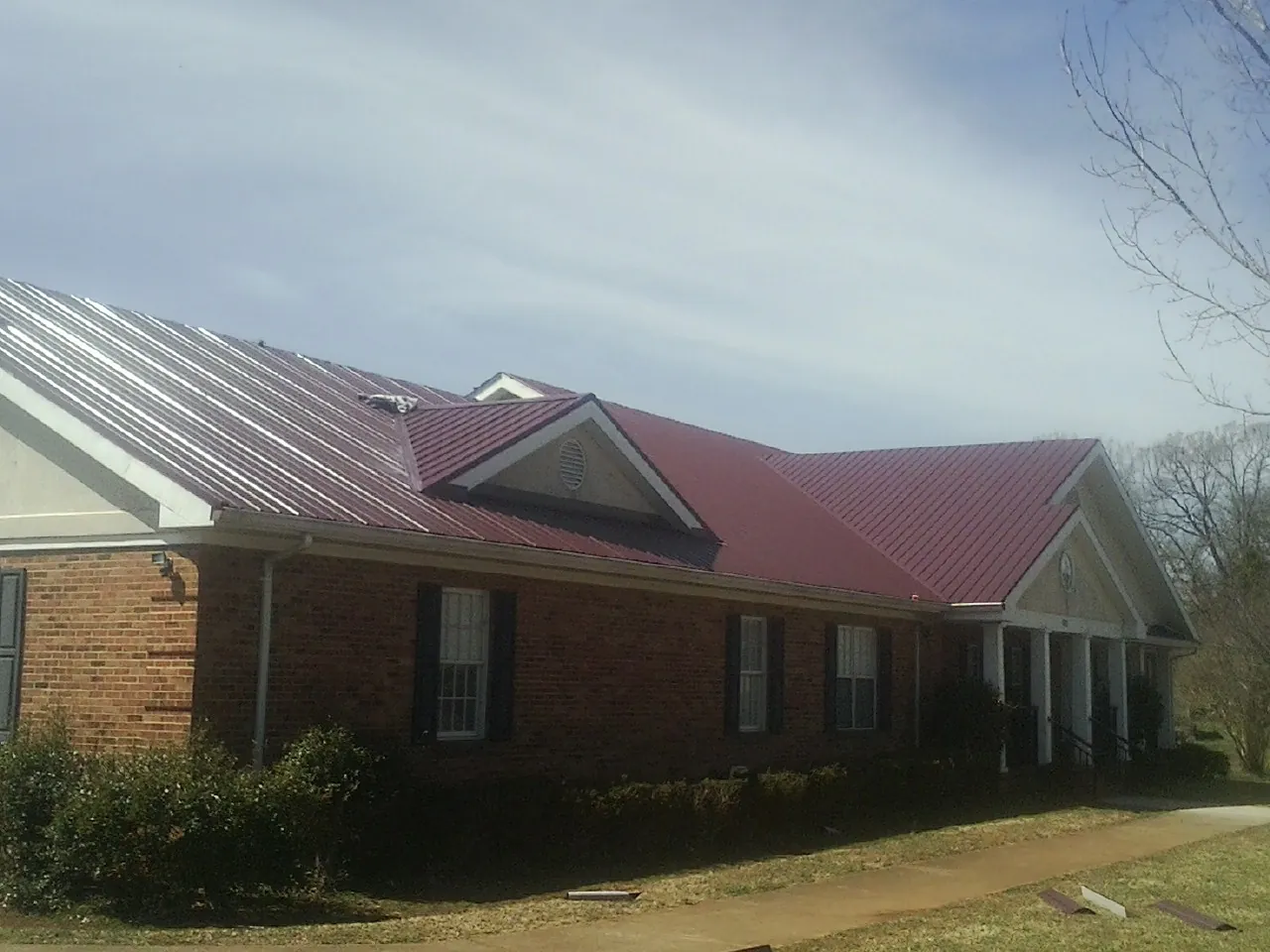 Red metal roof with gabled entries on a long brick building, from a Hail Damage Roof Repair job in Kershaw