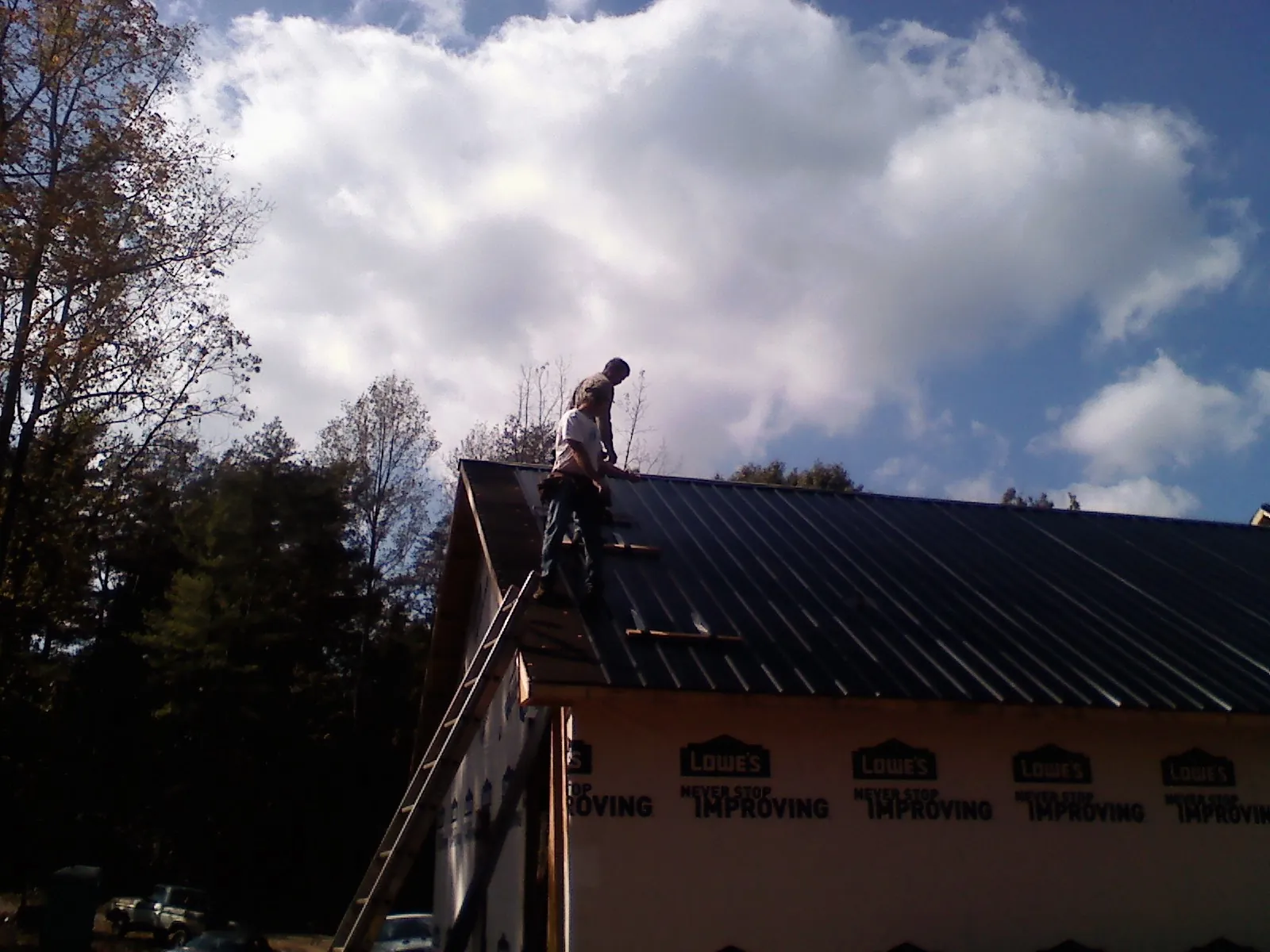 Roofer fastening dark metal panels high against a cloudy sky, from a Roof Inspection job in Kershaw
