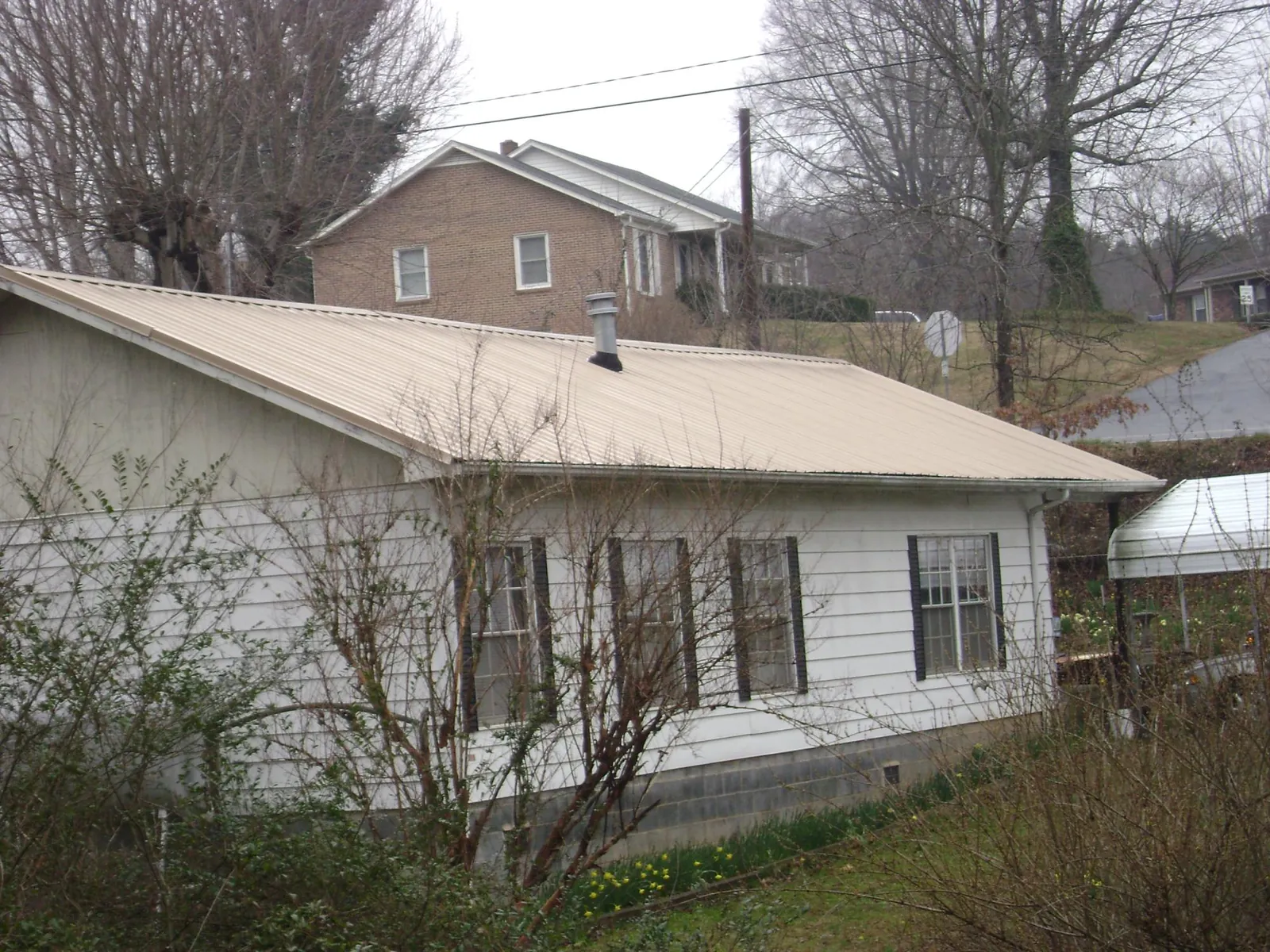 Tan metal roof on a white sided house set into a hillside — Commercial Roofing by Roofing Brothers in Kershaw