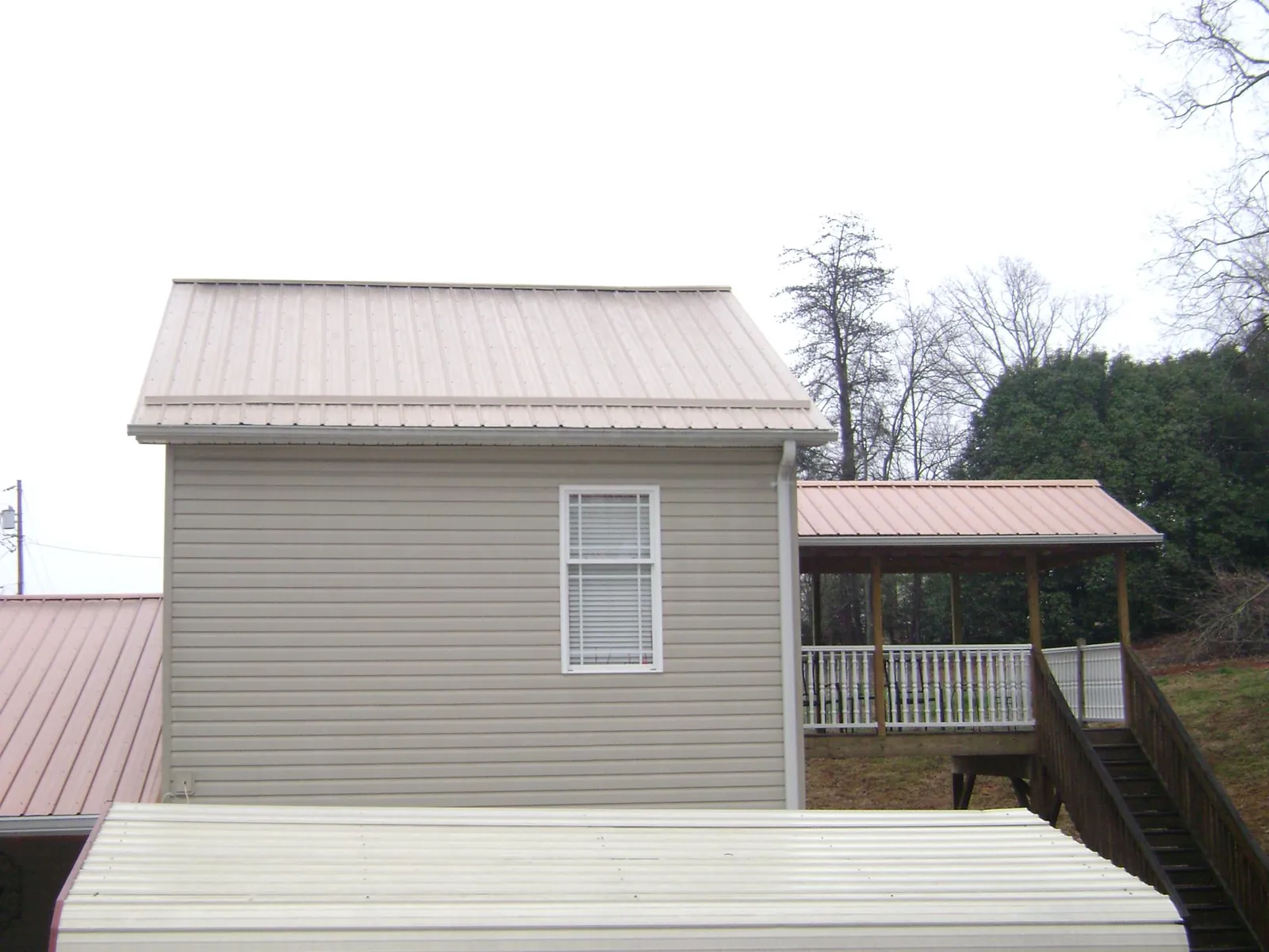 Tan metal roofs on a two story addition and attached porch, from a Roof Replacement job in Kershaw